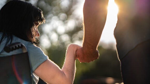 Close up of man and woman in wheelchair holding hands outdoors