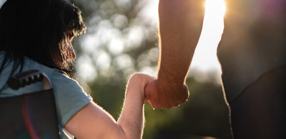 Close up of man and woman in wheelchair holding hands outdoors