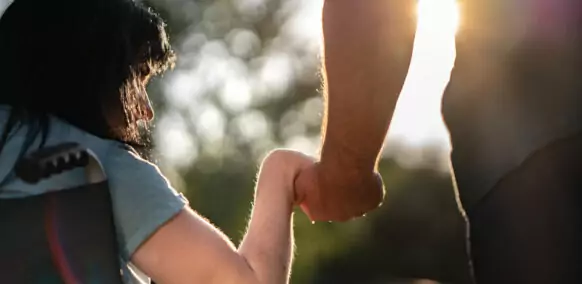 Close up of man and woman in wheelchair holding hands outdoors