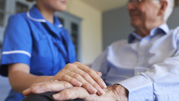 Nurse,Talking,With,Senior,Man,Sitting,In,Chair,On,Home