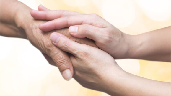 Caregiver, carer hand holding elder hand for hospice care. Philanthropy kindness to disabled old people concept with gold bokeh background.Happy mother's day.