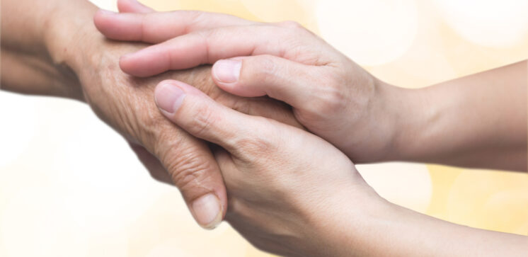 Caregiver, carer hand holding elder hand for hospice care. Philanthropy kindness to disabled old people concept with gold bokeh background.Happy mother's day.